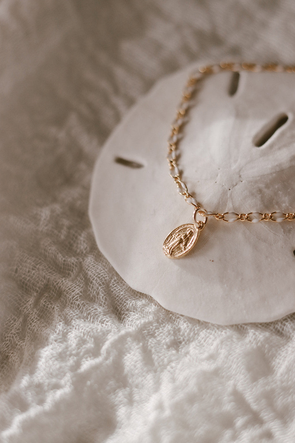 Close-up of gold Miraculous Medal charm on white scalloped backing