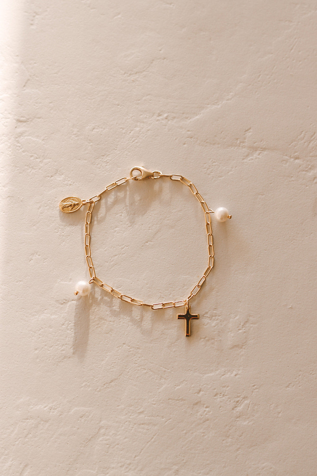Gold link bracelet with white pearl beads and a small cross charm