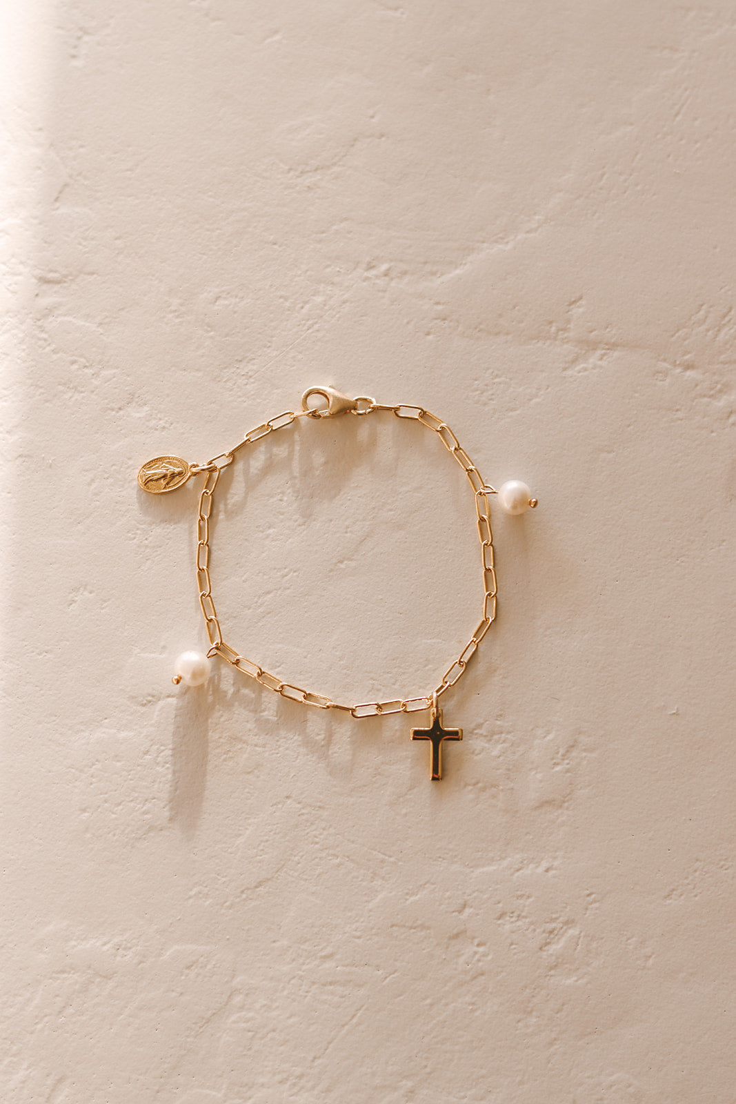 Gold link bracelet with white pearl beads and a small cross charm