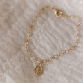 Gold chain bracelet with oval Miraculous Medal charm, laid on soft fabric