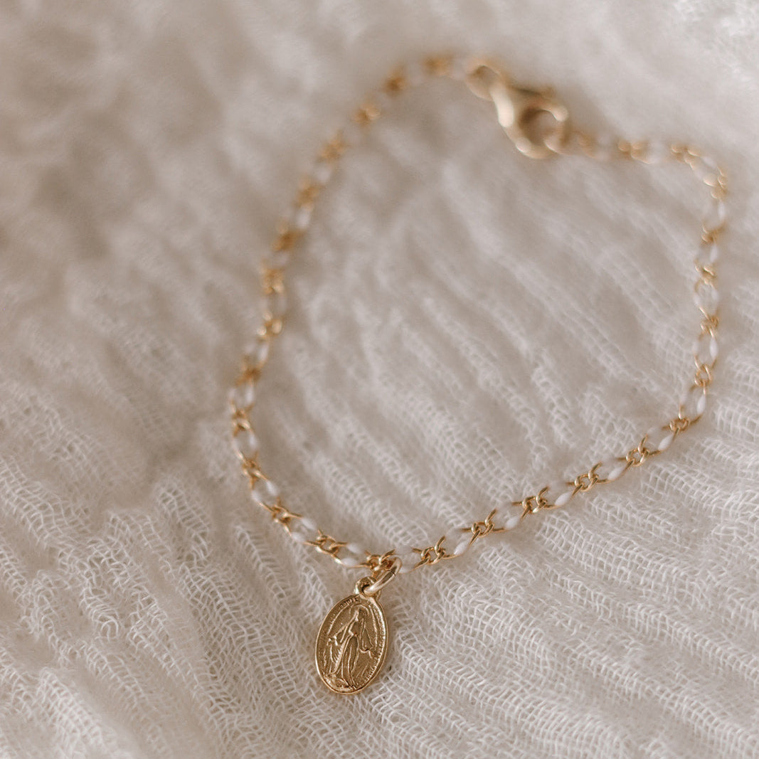 Gold chain bracelet with oval Miraculous Medal charm, laid on soft fabric