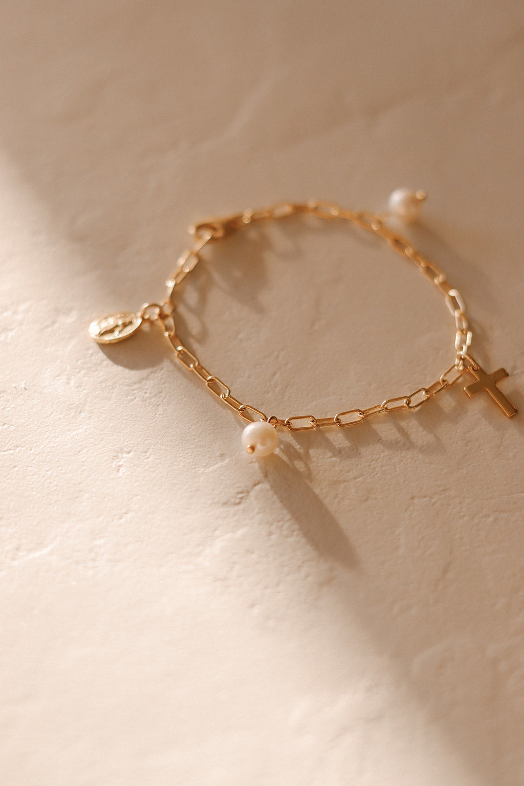 Gold link bracelet with pearl beads and cross charm, laid on white surface