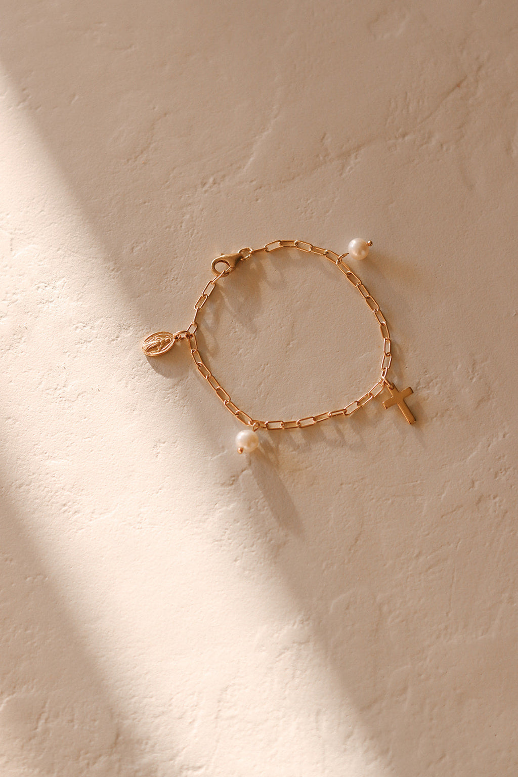 Gold-tone bracelet with heart charm, cross charm, and white pearl bead accents