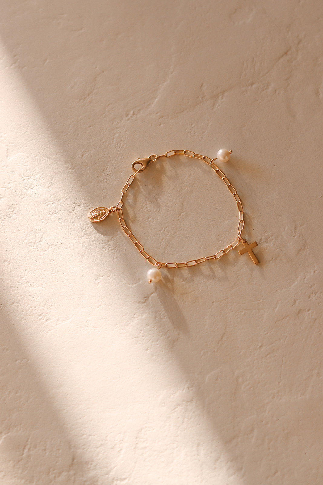 Gold-tone bracelet with heart charm, cross charm, and white pearl bead accents