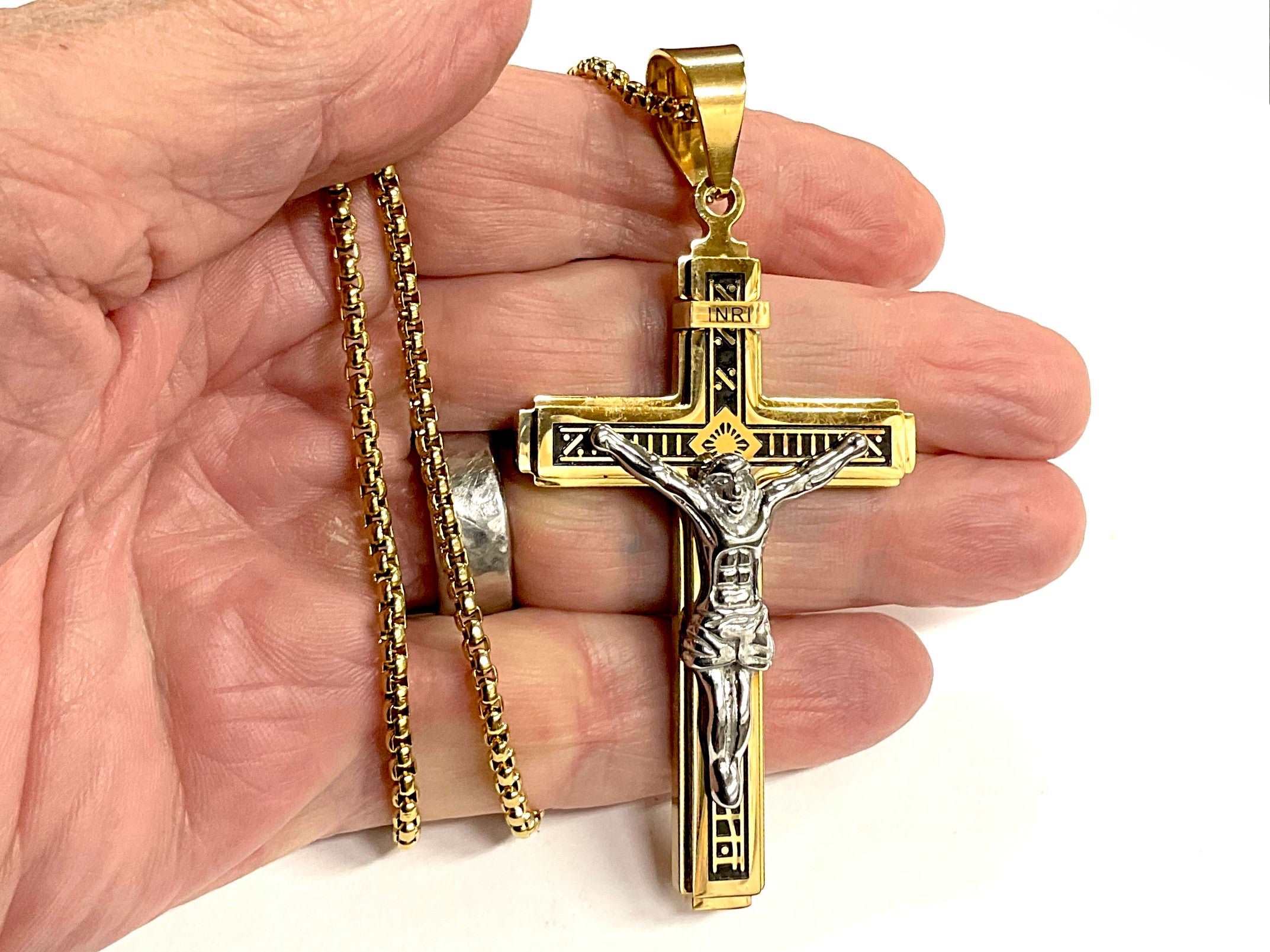 Silver-and-gold gothic cross pendant on metal chain, held in hand for display