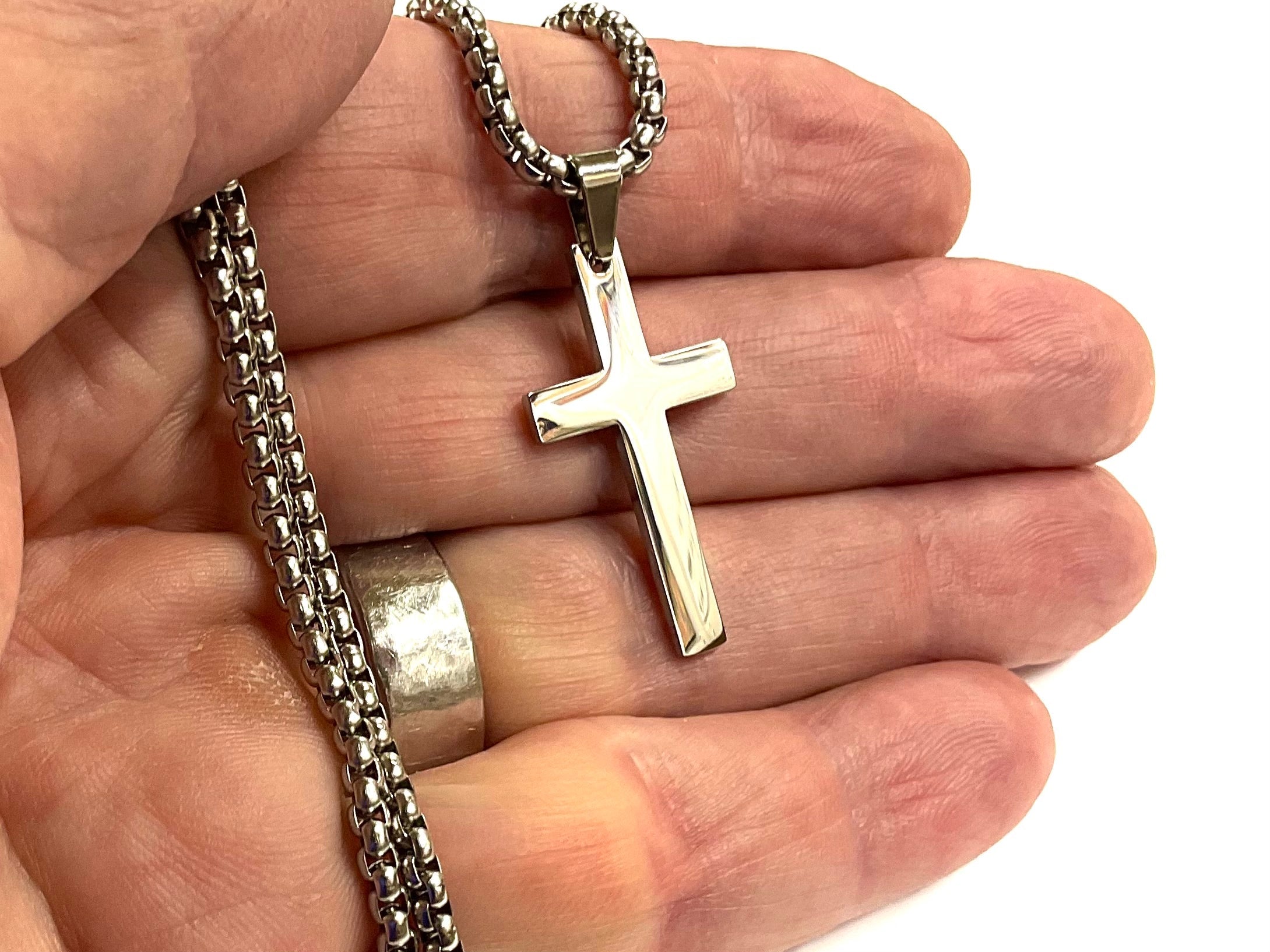 Cross pendant necklace held in hand with silver link chain