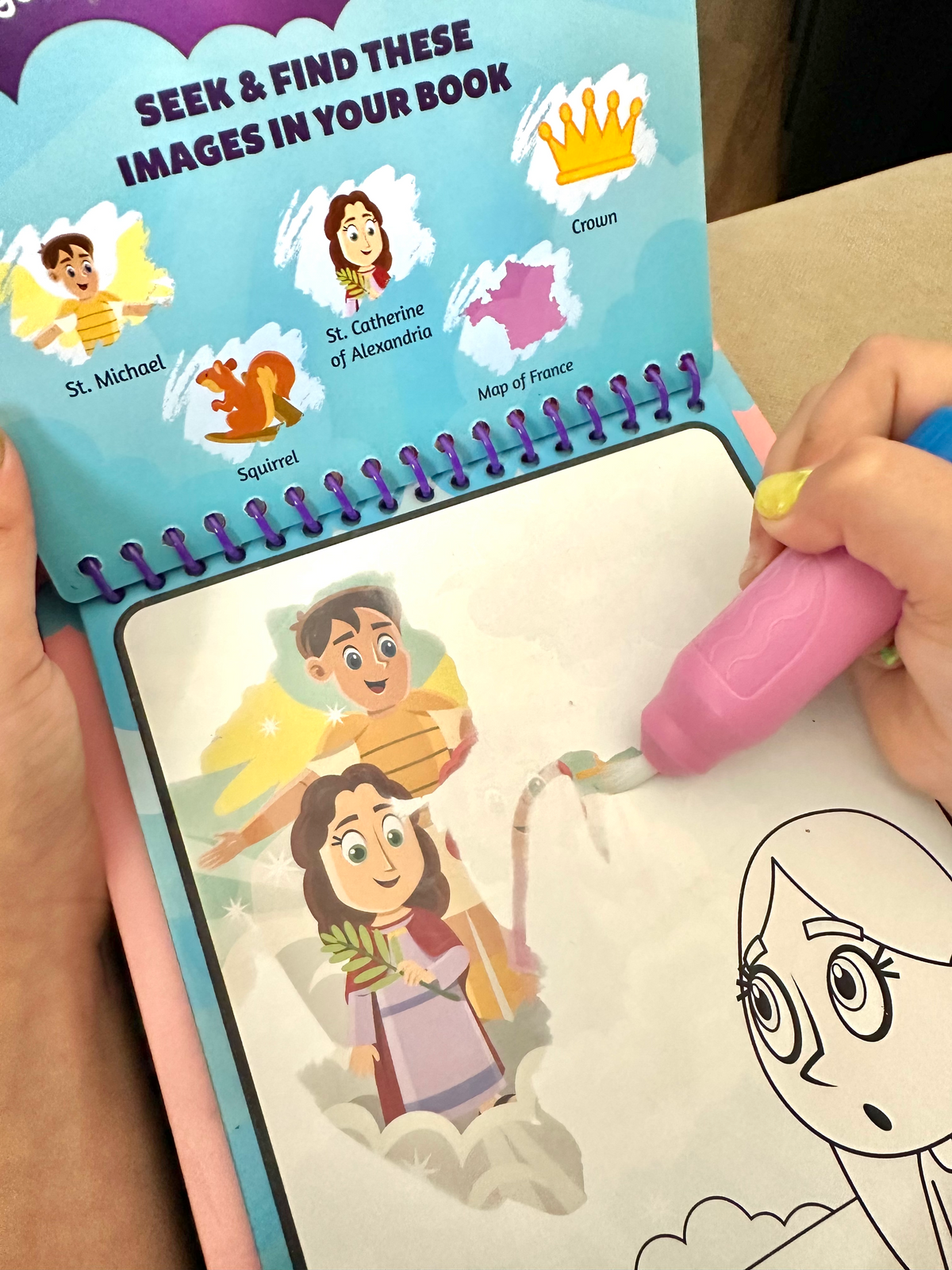 Kids spiral coloring book page with seek-and-find characters and pink marker in use