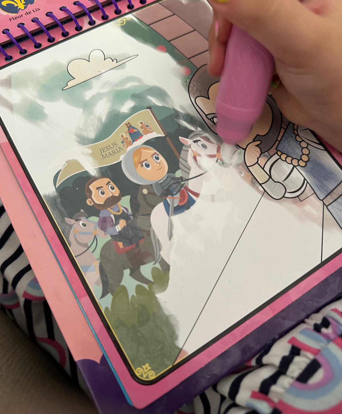 Kids coloring book page being colored with pink marker showing a saint and angel figures