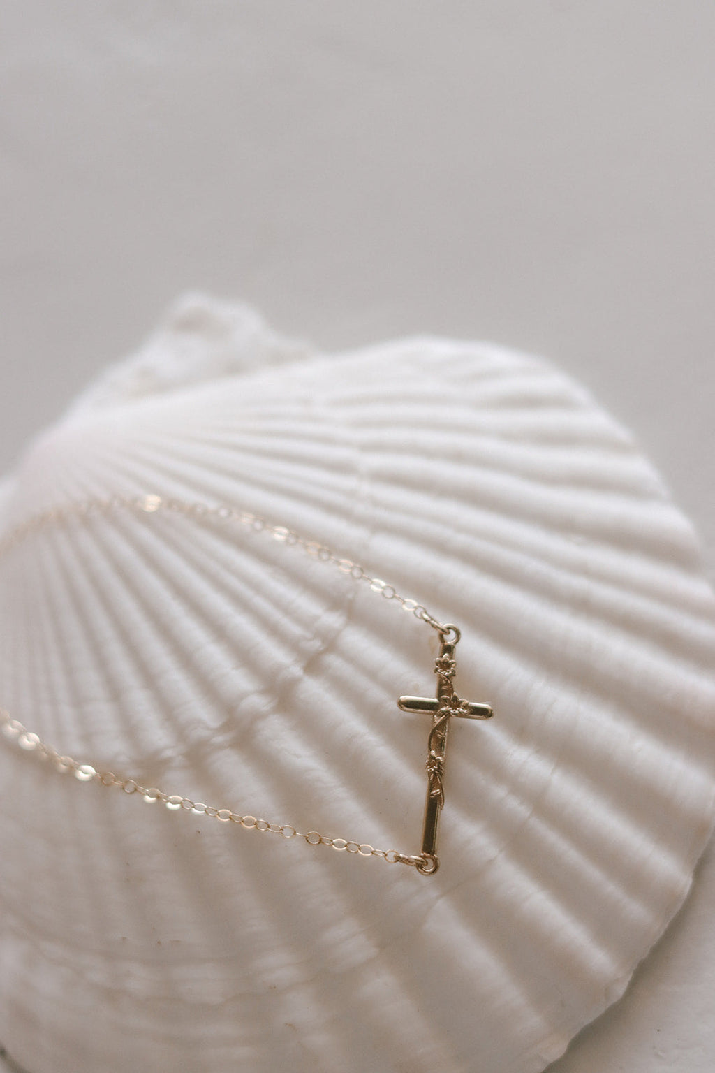 Close-up of gold-tone bracelet chain with vertical cross charm on a seashell