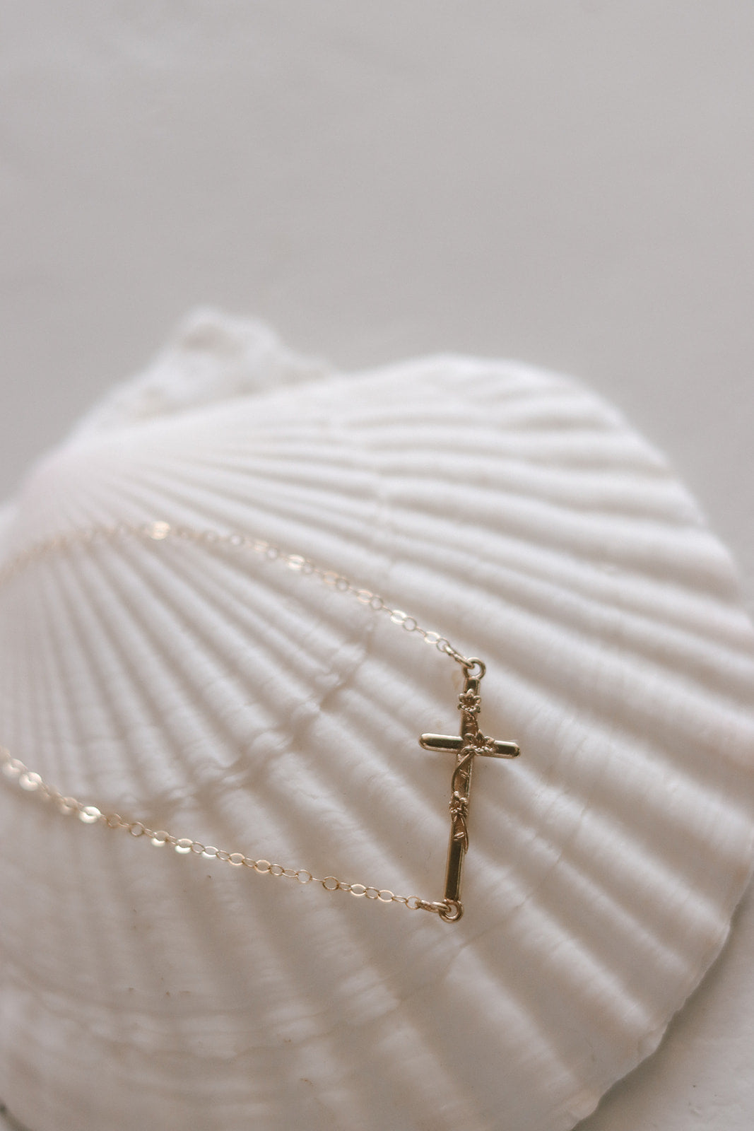 Close-up of gold-tone bracelet chain with vertical cross charm on a seashell