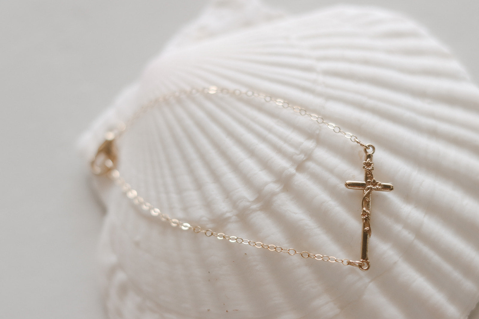 Gold-tone chain bracelet with small cross charm on a white seashell