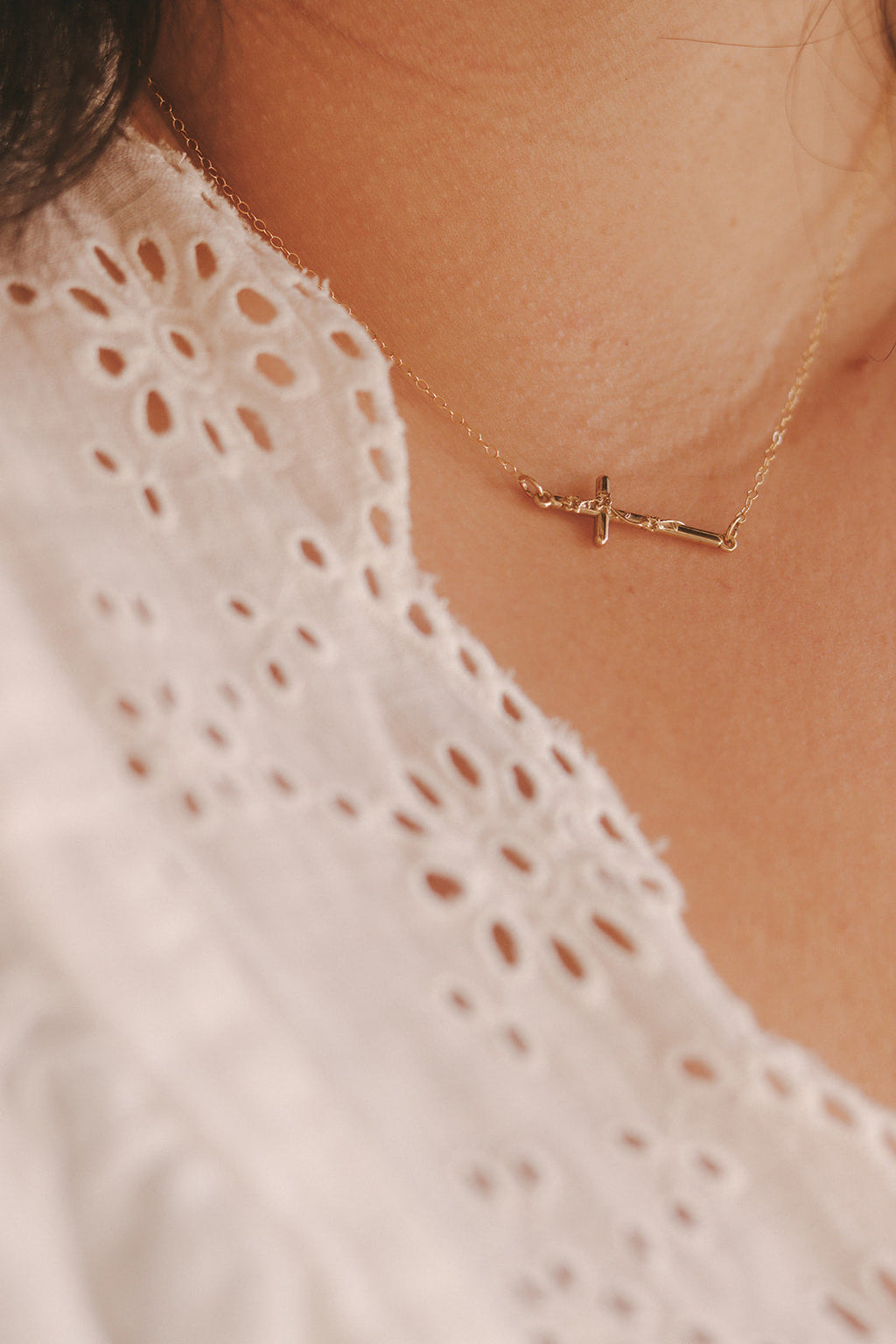 Gold-tone cross pendant necklace on skin with a gold short chain and delicate clasp.