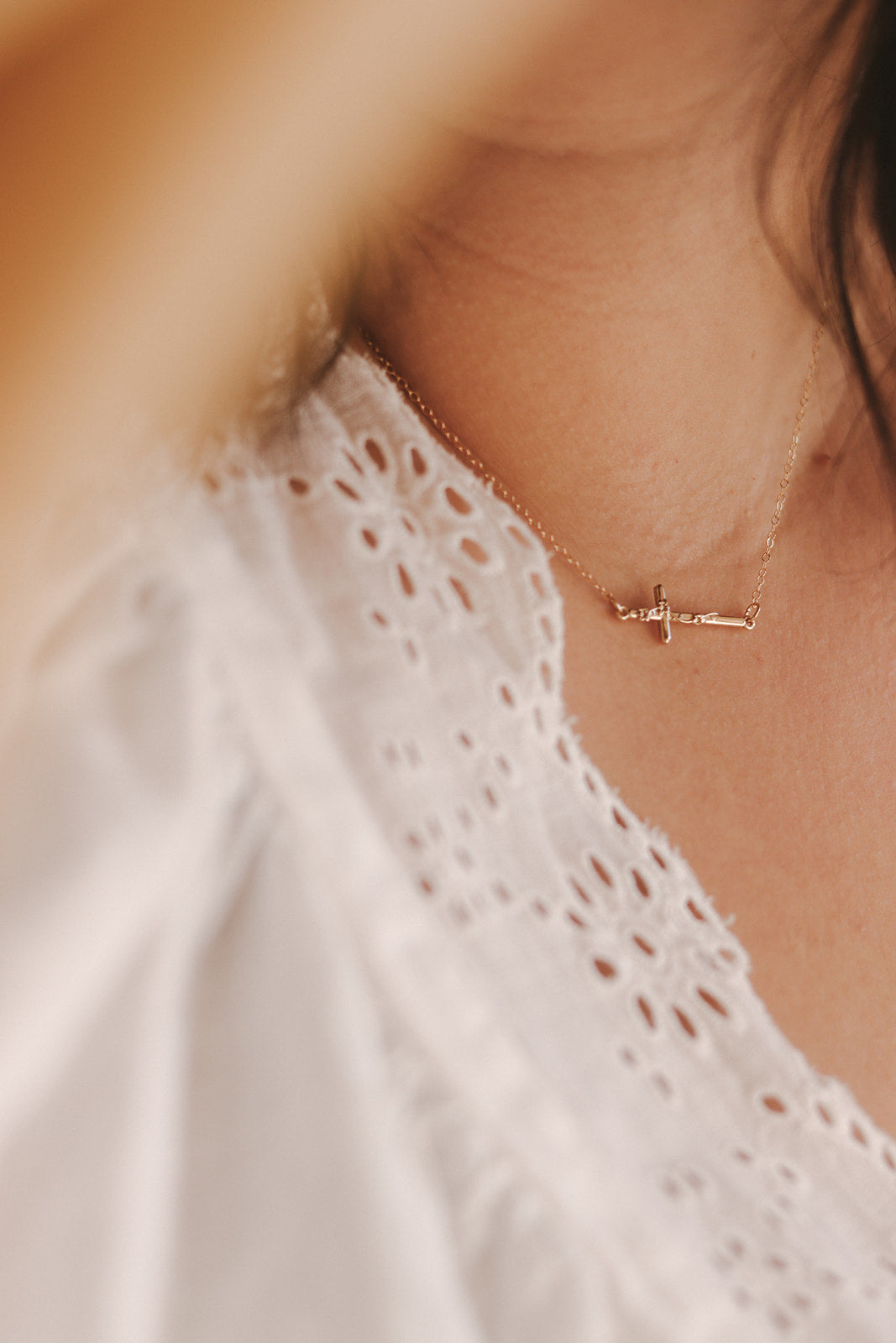 Gold-tone cross pendant necklace on neck and collarbone with white eyelet fabric.