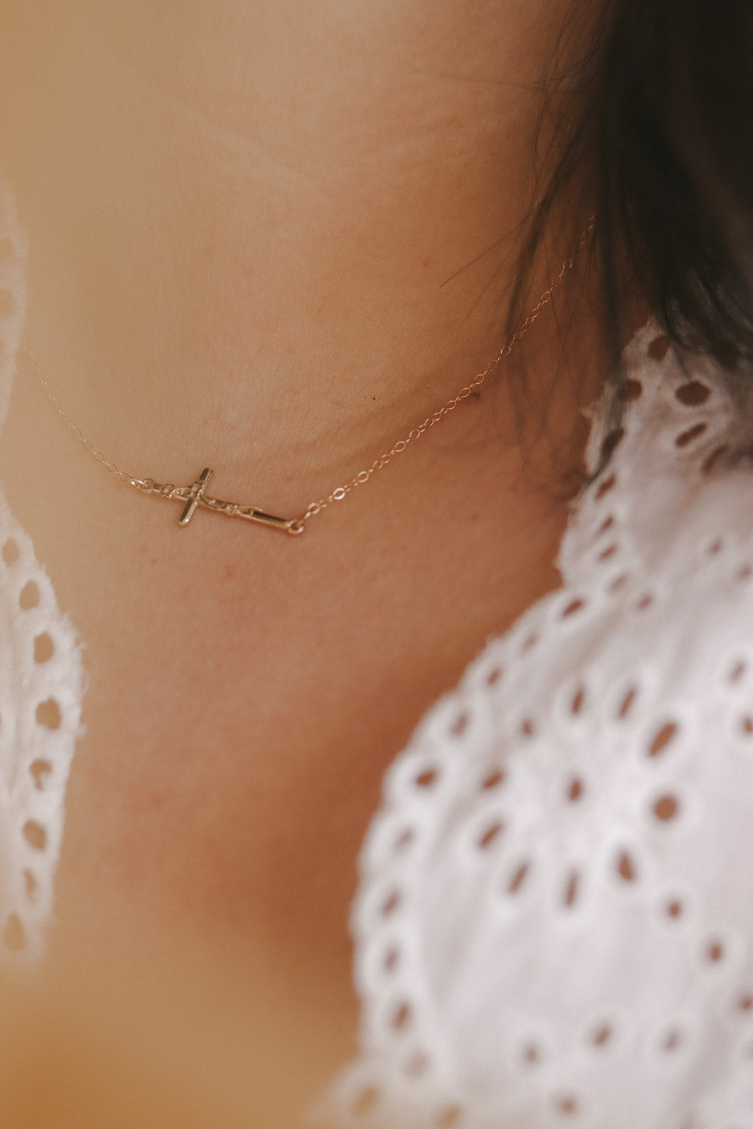 Gold-tone cross pendant necklace on skin, viewed from collarbone level with white fabric edge.