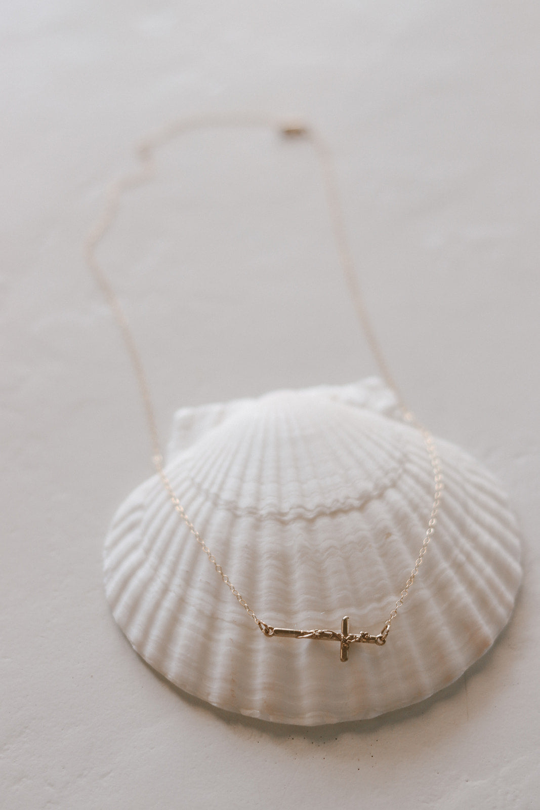 Gold-tone cross pendant necklace on a white shell dish, shown with the full chain.