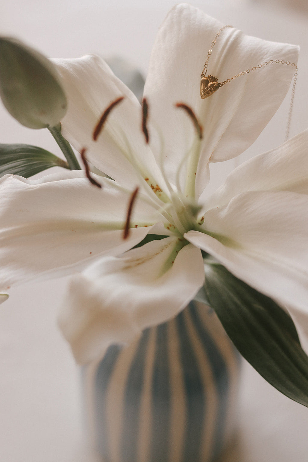 Gold heart pendant necklace with delicate chain against a white lily flower