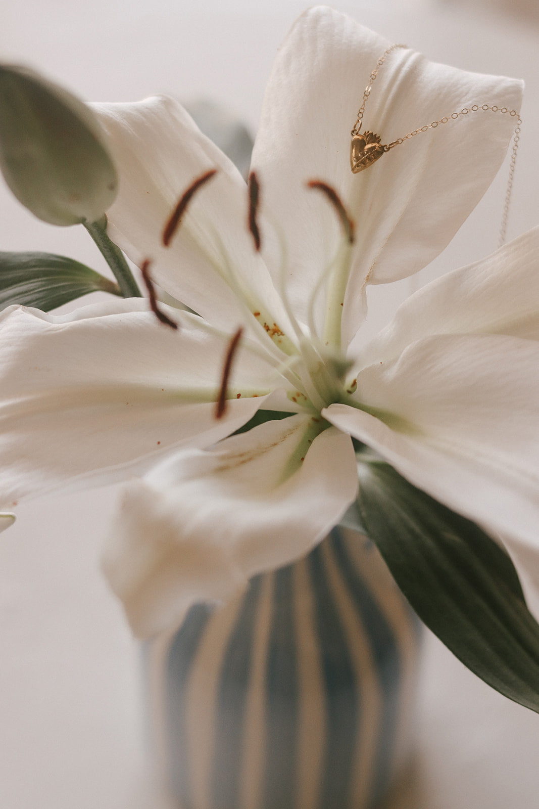 Gold heart pendant necklace with delicate chain against a white lily flower