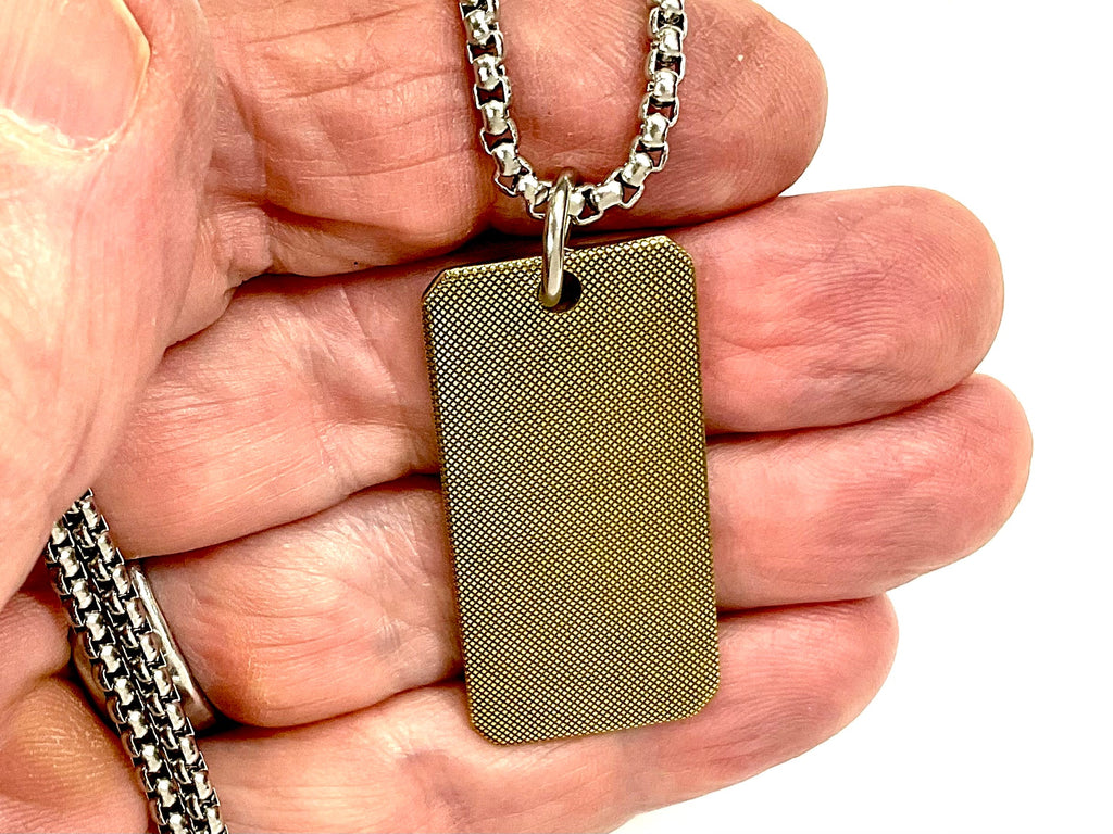 Gold-tone flat dog tag cross pendant with 'BELIEVE' text, shown close-up in hand