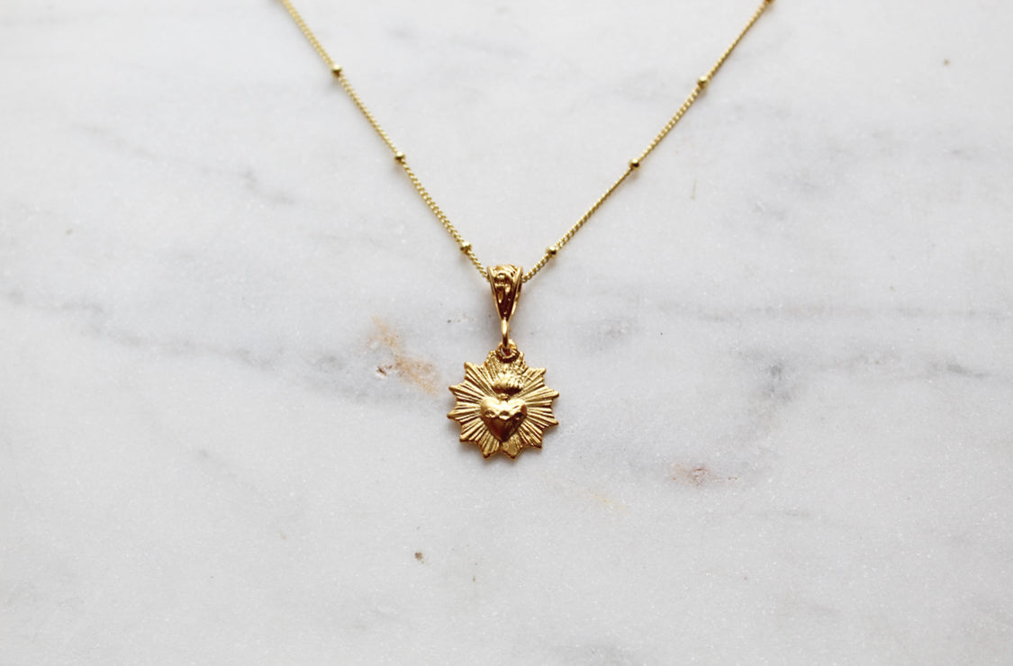 Scalloped necklace with gold sunburst charm on thin chain, small clasp at top