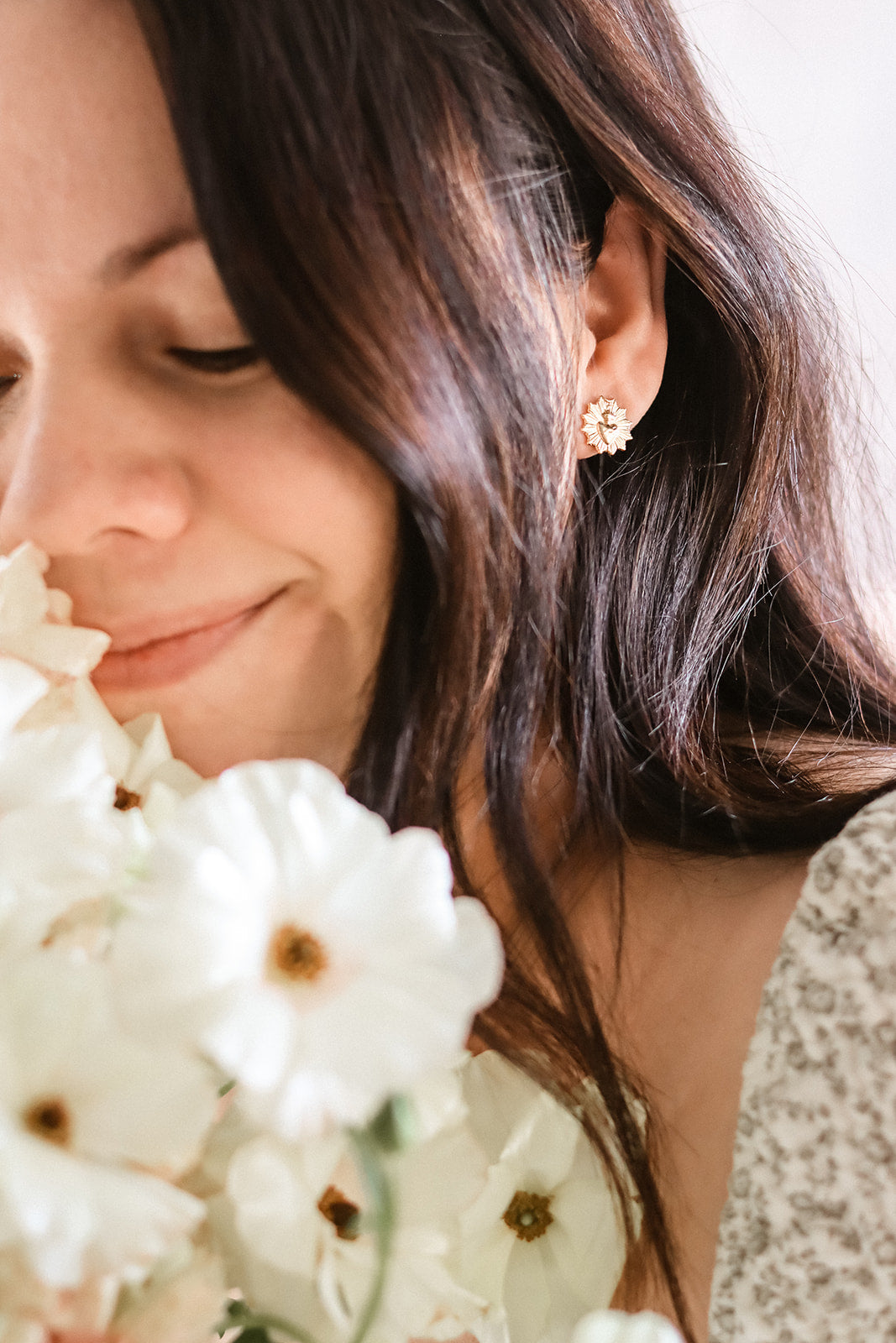 Gold-toned sacred heart stud earrings on model, small floral cross motif, pair
