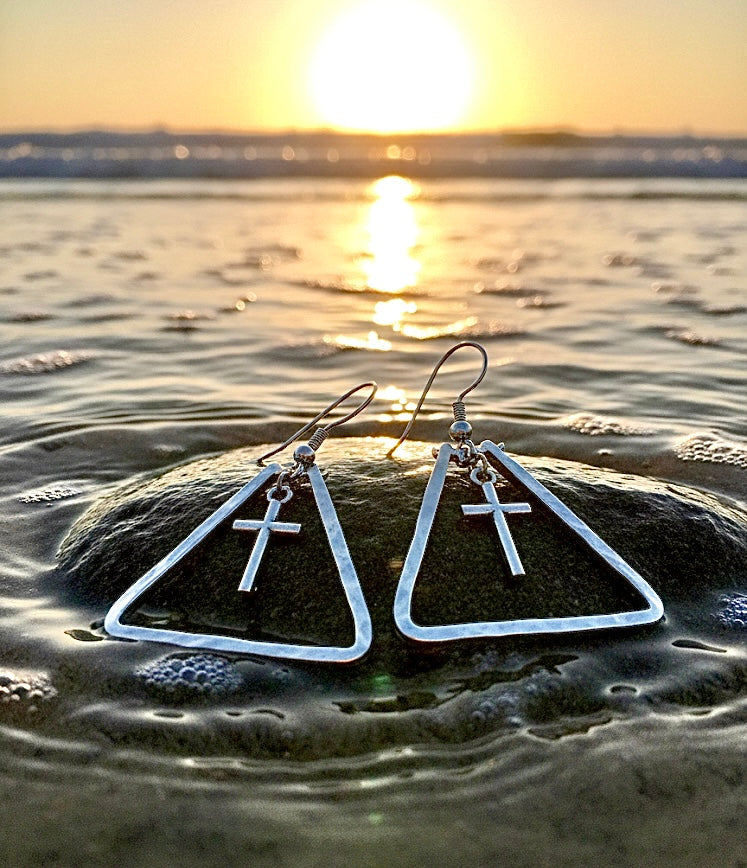 Silver triangle dangle cross earrings on wet sand with hook back