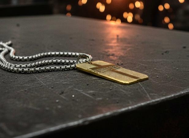 Gold-tone dog tag cross pendant on silver-tone box chain, resting on surface