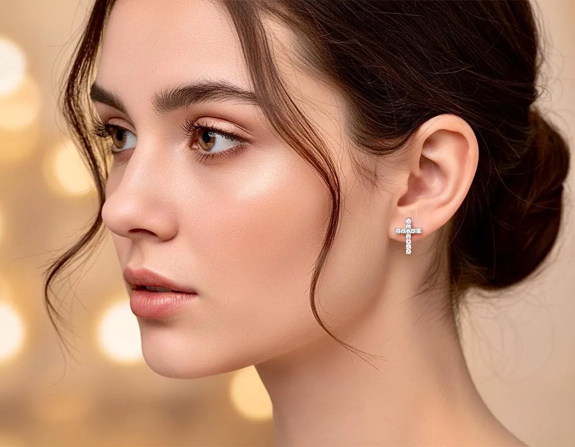 Small cross stud earrings with clear crystal details, shown on the ear