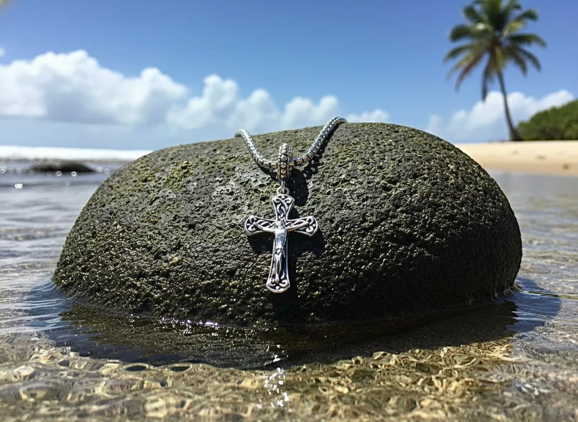 Silver crucifix pendant on a chain, resting on a dark stone.