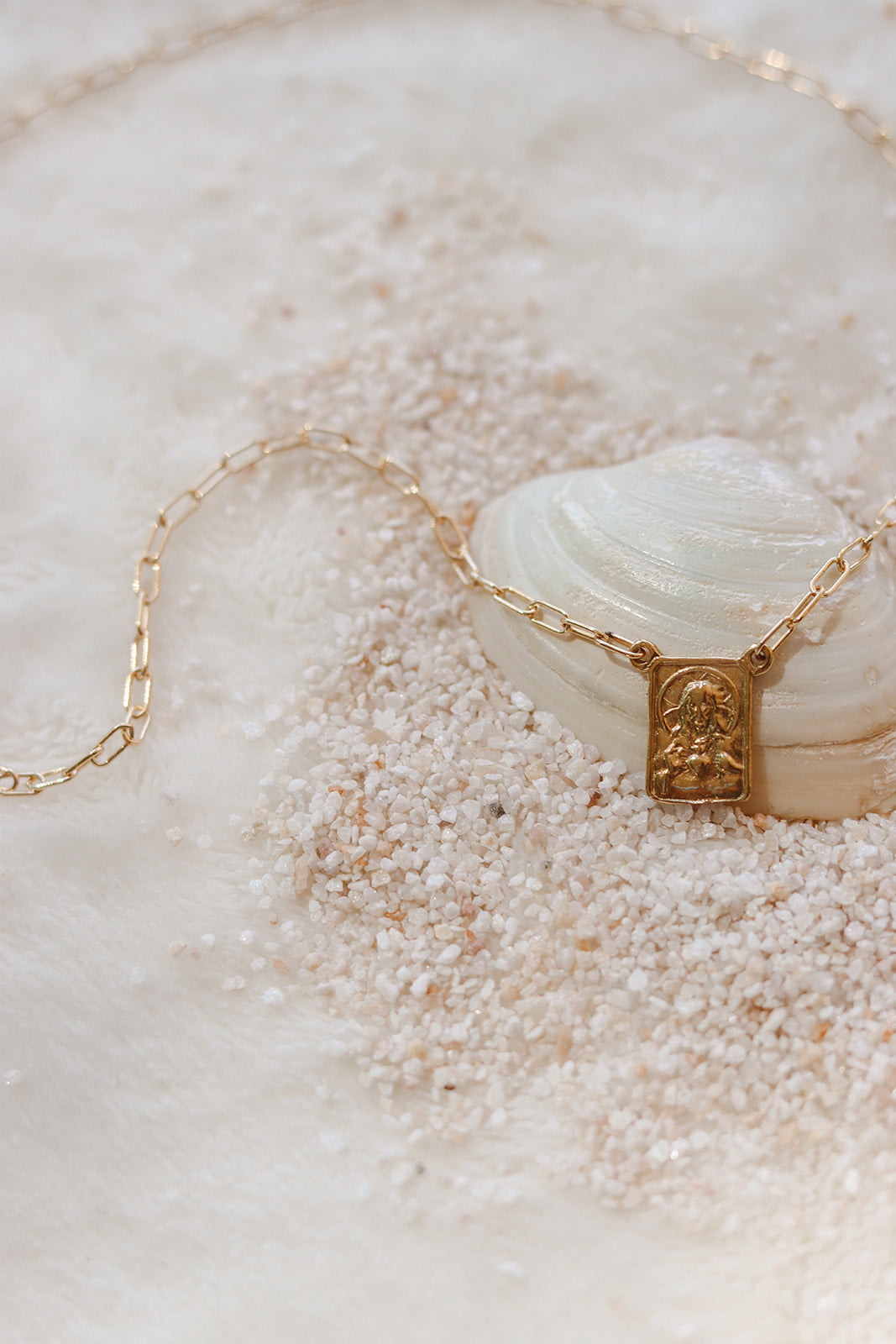 Gold paperclip scapular necklace with square pendant and chain on shell