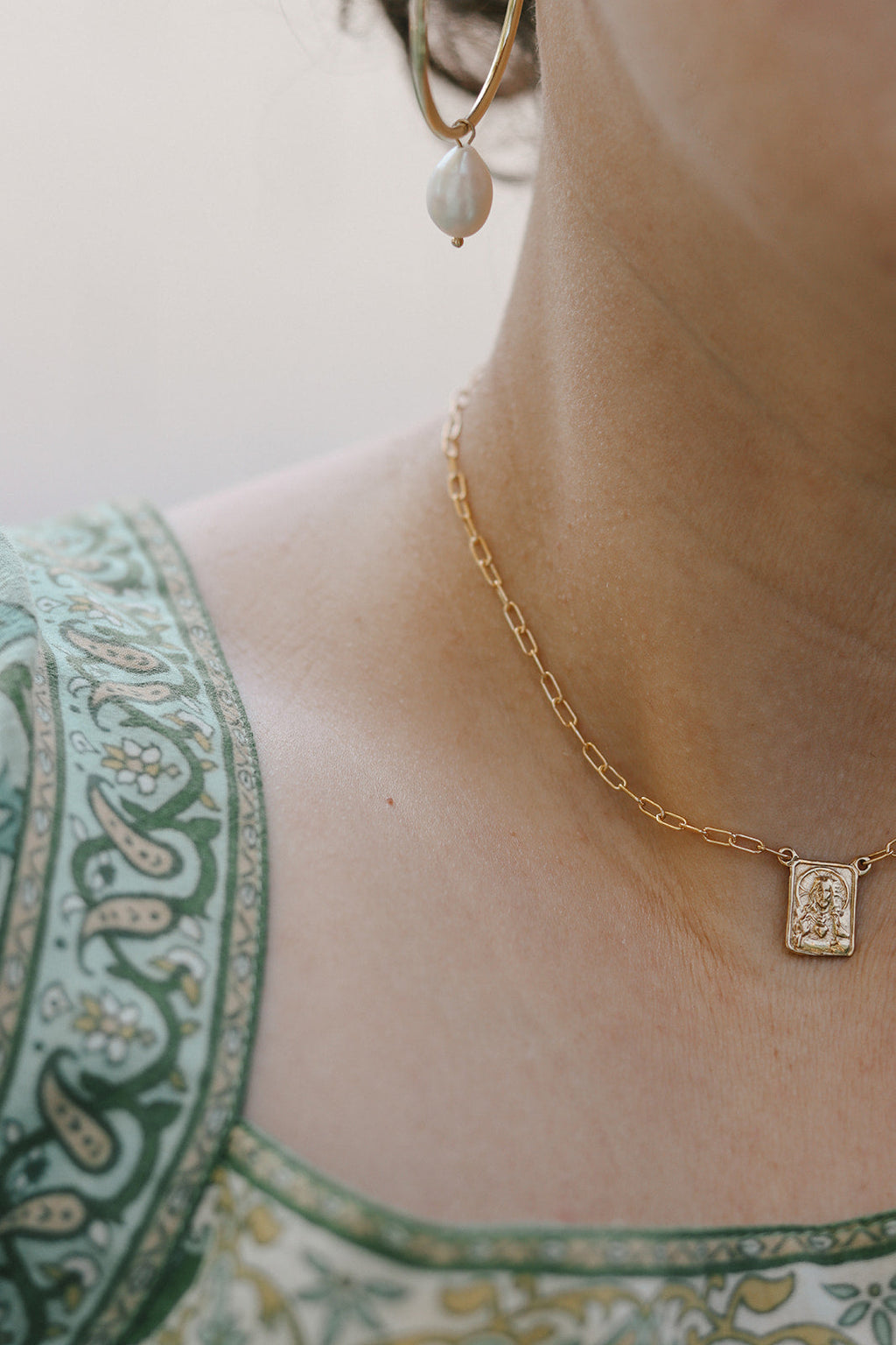Gold paperclip scapular necklace with square pendant worn near collarbone