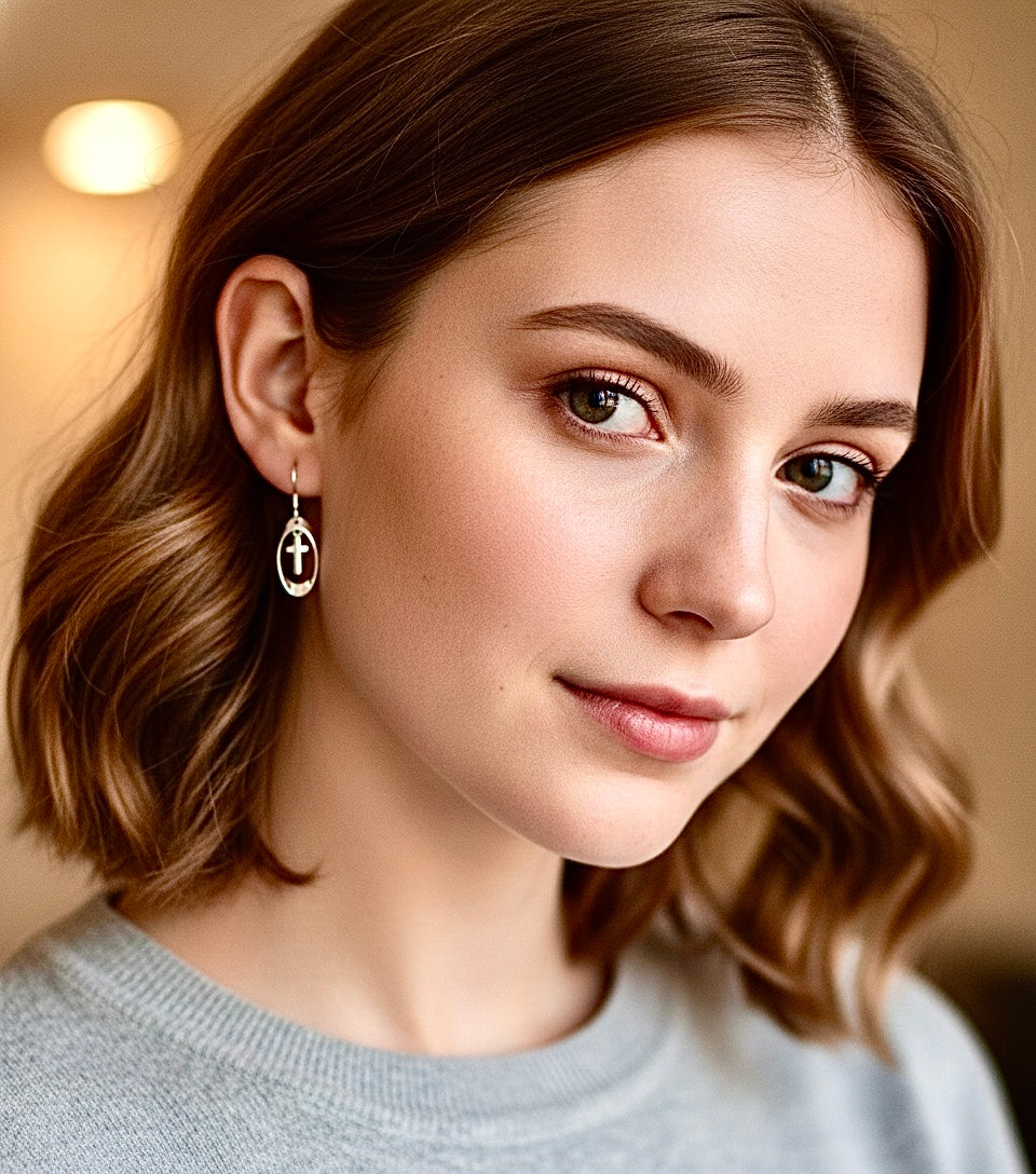 Silver cross drop earrings with oval hoops, worn on a model