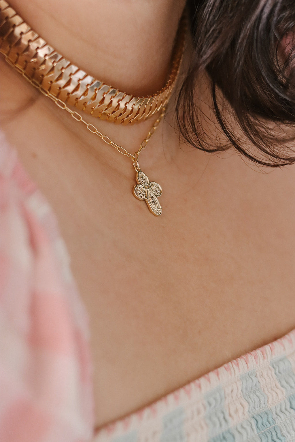 Gold paperclip chain necklace with small cross charm at collarbone