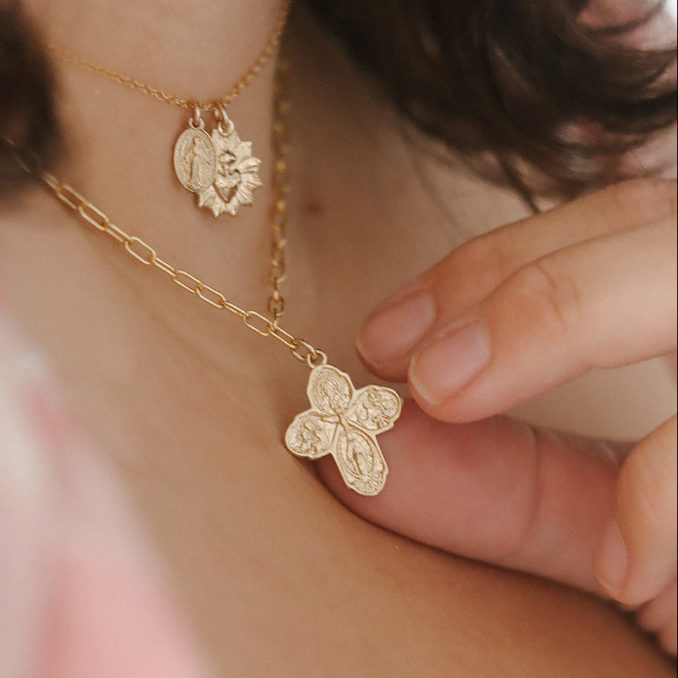 Gold paperclip chain necklace with four-leaf cross pendant held in hand