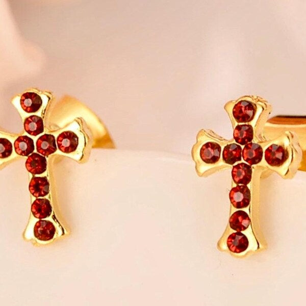 Gold cross stud earrings with red CZ stones, partial close-up showing earring shape
