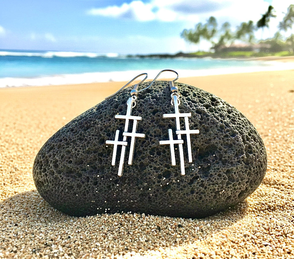 Silver triple cross drop earrings resting on a stone, two stacked cross motifs