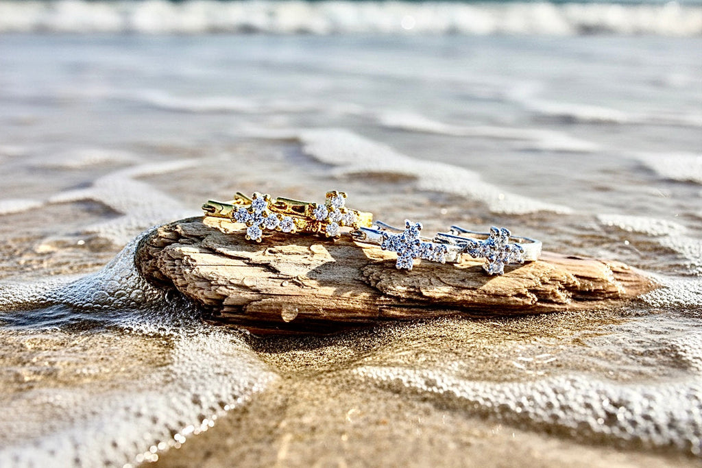 Cross huggie earrings with clear CZ stones, gold and silver tones, on beach rocks.