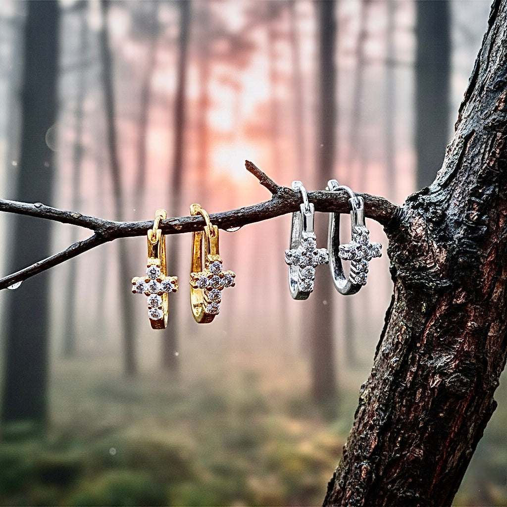 Cross huggie earrings with clear CZ crosses, gold and silver tones, hanging from branches.