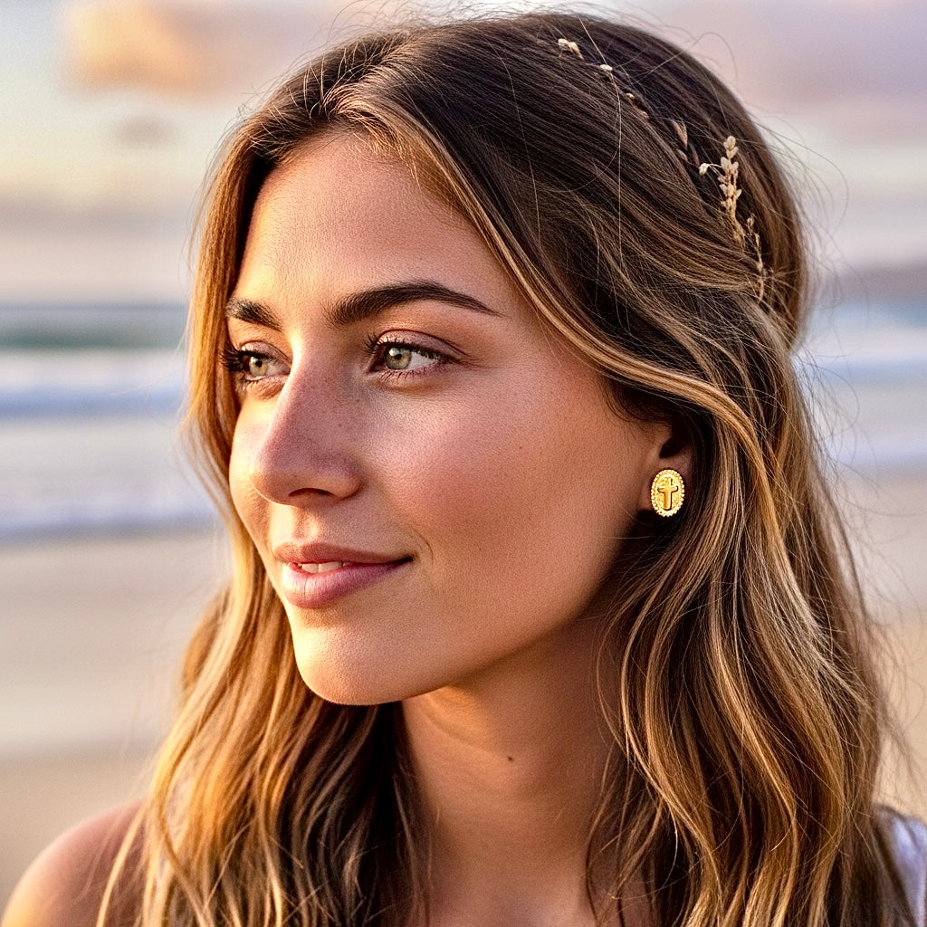 Gold oval cross stud earrings on a woman’s ear