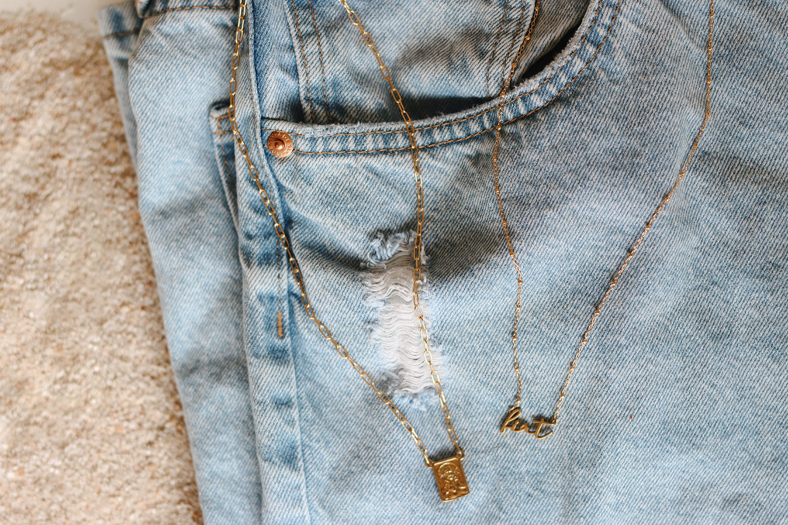 Scapular charm necklace on light blue denim with gold-tone chain and bar charms
