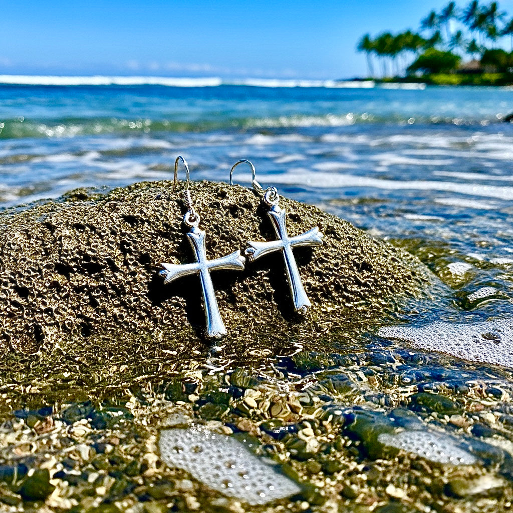Sterling silver cross dangle earrings with shiny cross charms on a rocky shoreline
