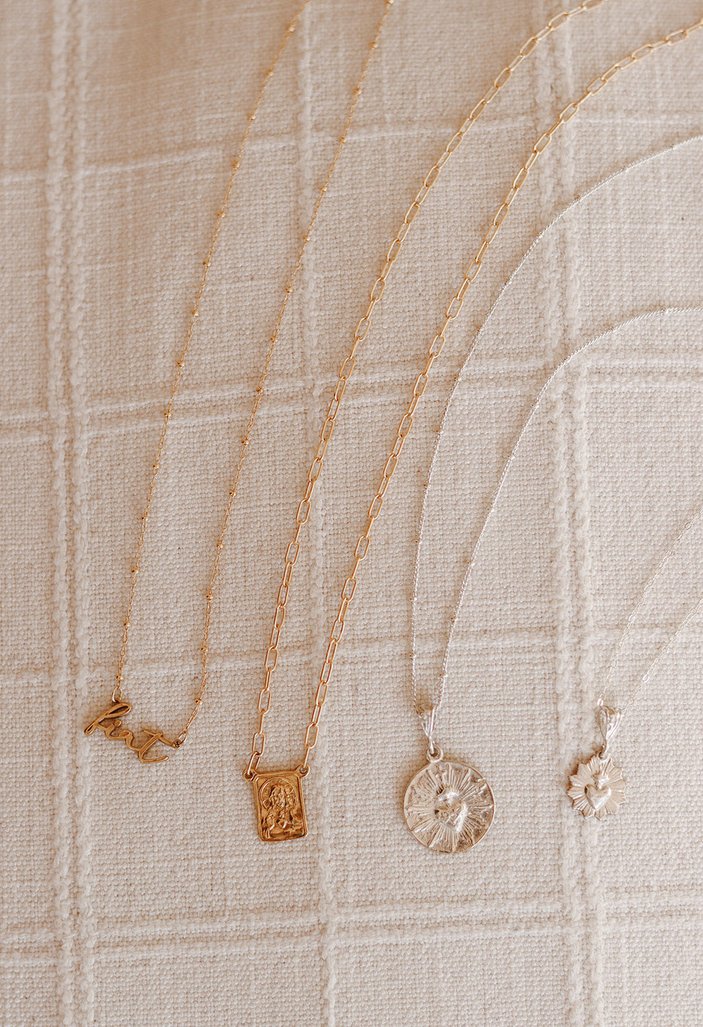 Gold- and silver-tone charm necklace set on light fabric, with a round coin charm.