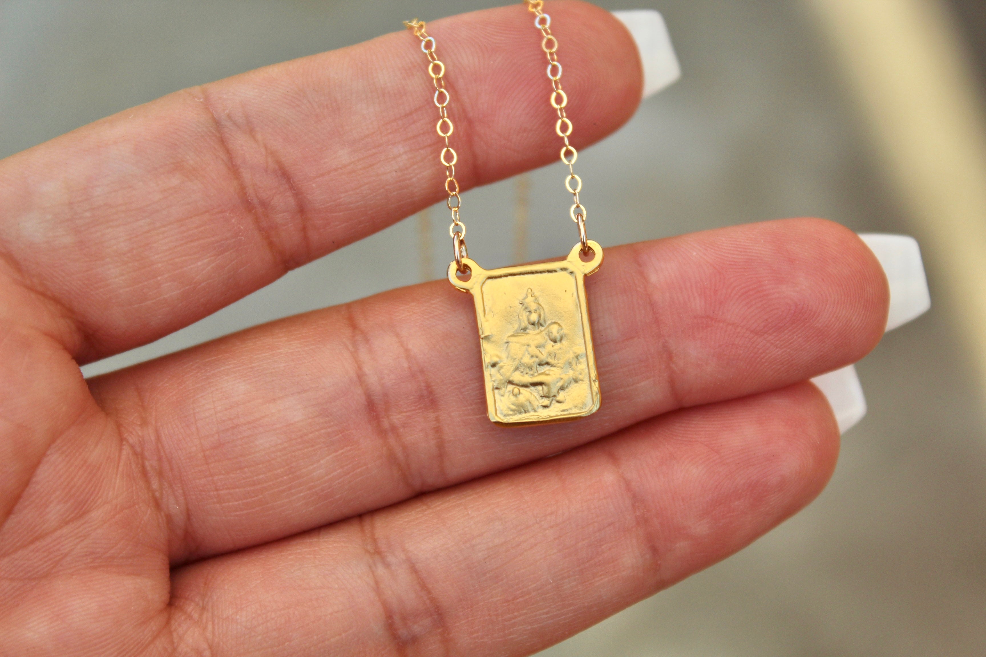 Gold-tone scapular pendant necklace with square charm and round link chain, hand-held.