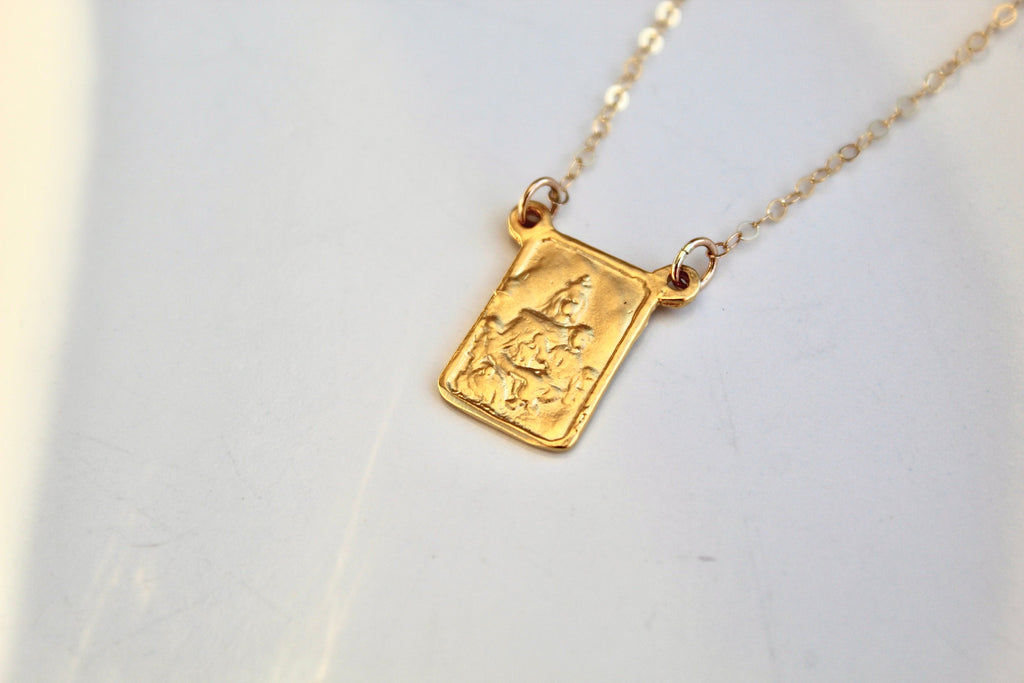 Gold-tone scapular necklace with square pendant charm and fine chain, laid flat.