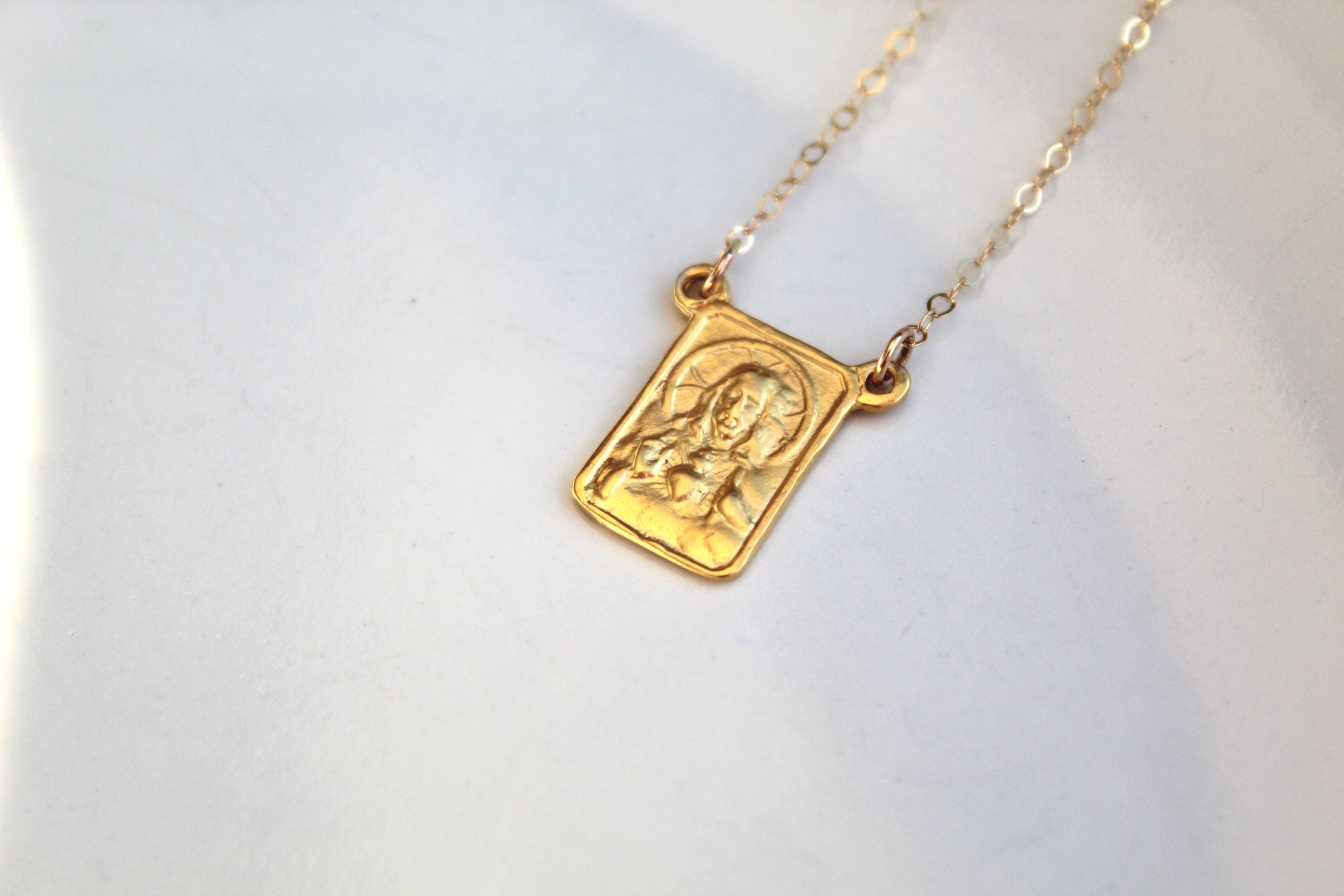 Gold-tone scapular necklace with square pendant and chain, flat relief figure design.