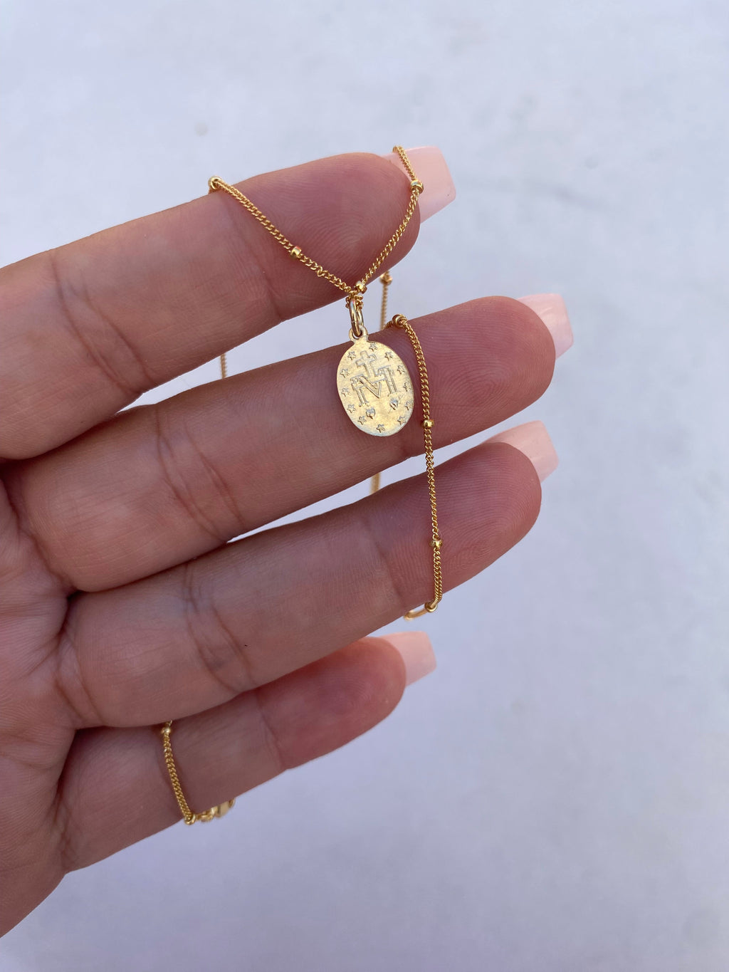 Gold-tone chain necklace held in hand with round medal pendant