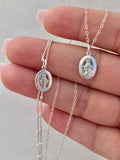 Silver miraculous medal necklace with oval pendant and linked chain, on hand close-up