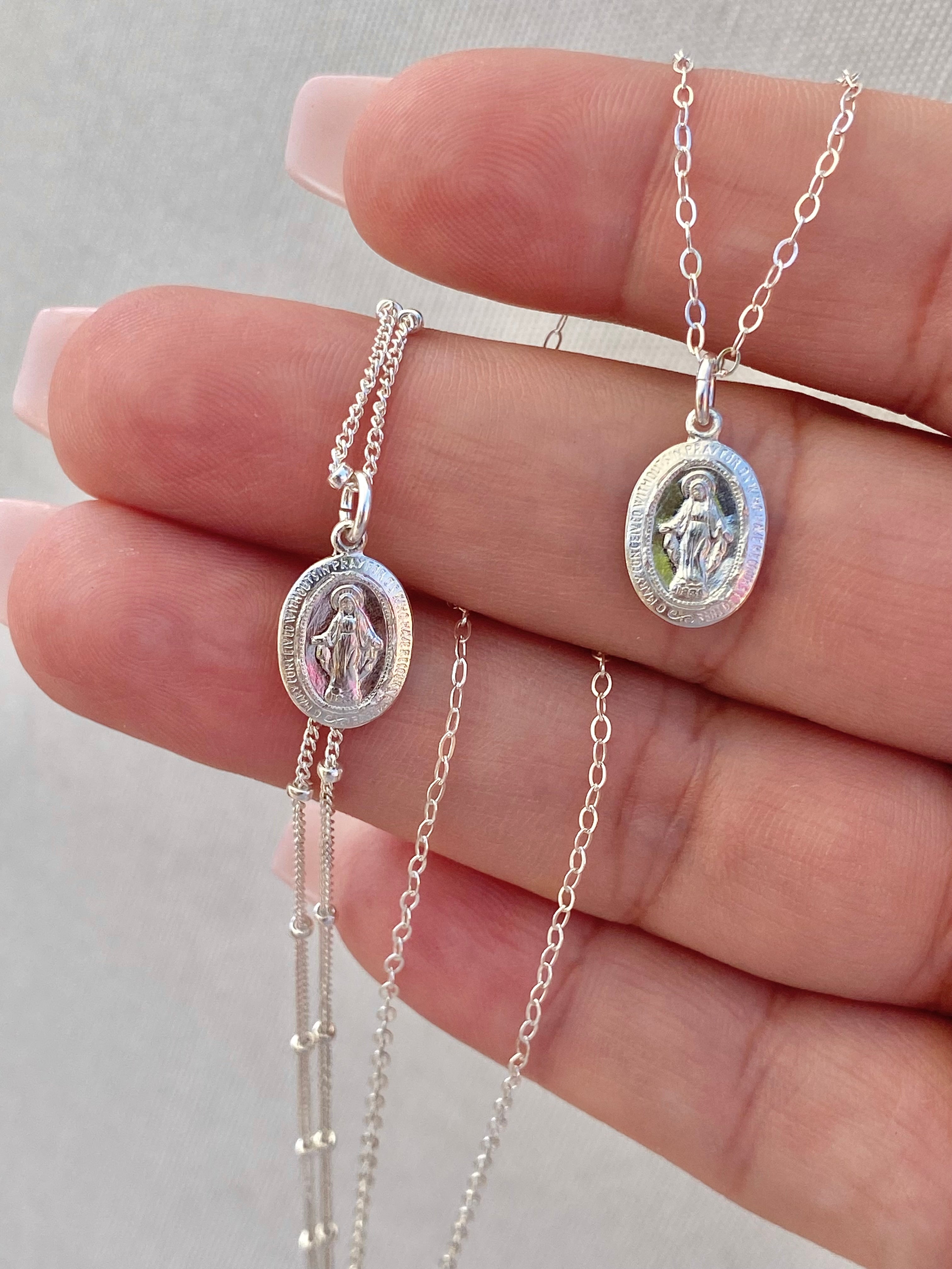 Silver miraculous medal necklace with oval pendant and linked chain, on hand close-up