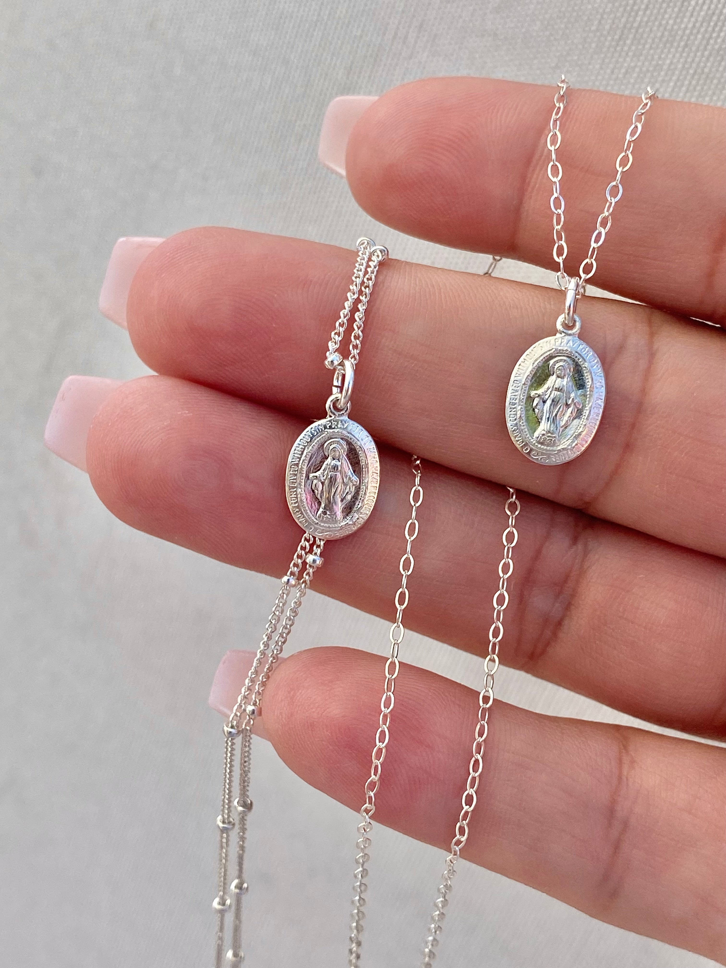 Silver miraculous medal necklace on chain, shown on hand with oval pendants