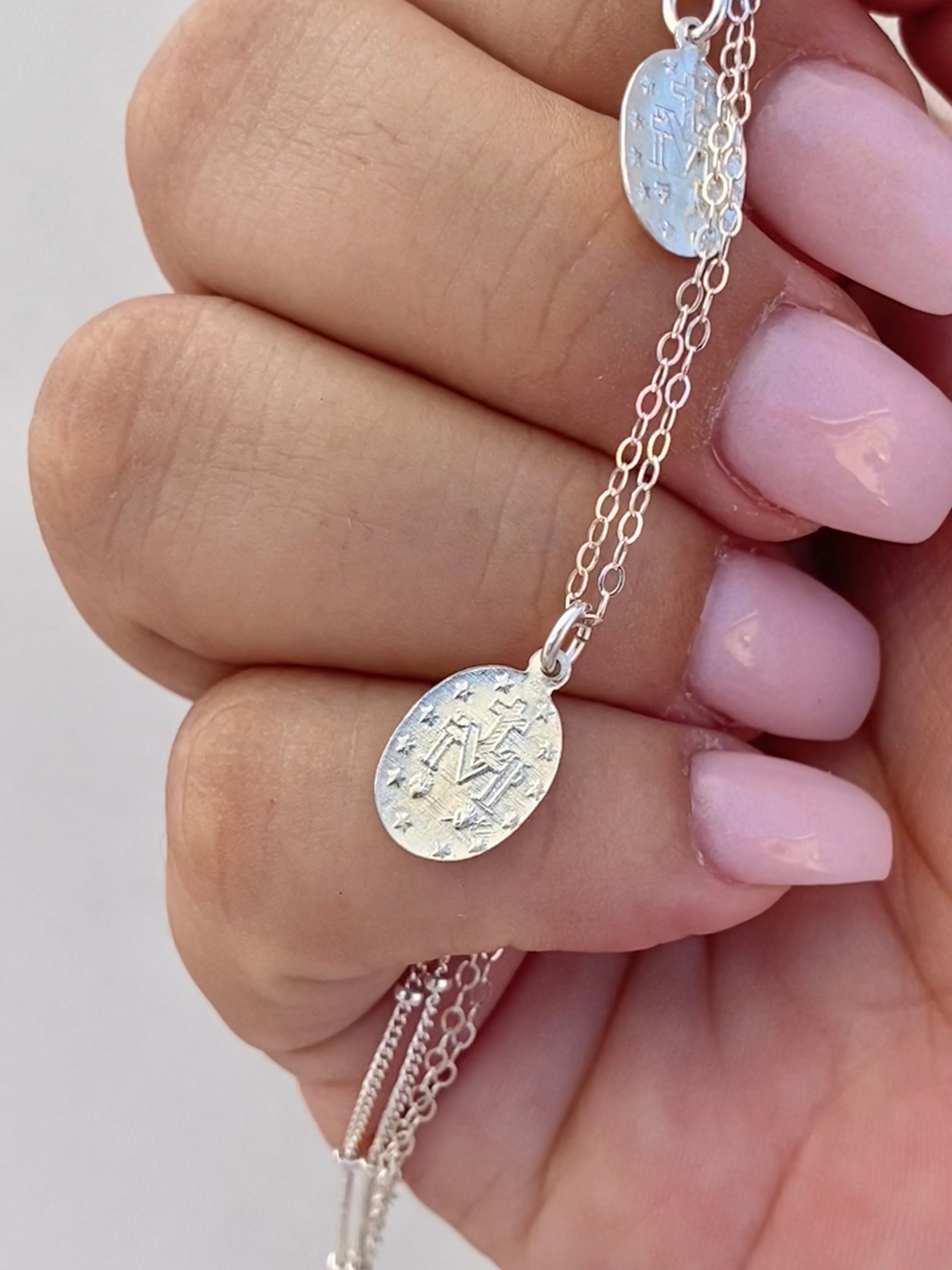 Silver medal pendant necklace with oval medallion and fine chain, held in hand