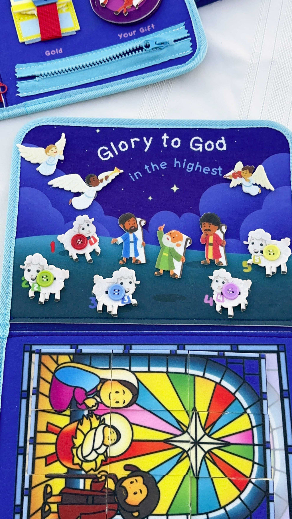 Nativity busy book open page reading “Glory to God” with felt animal and angel characters